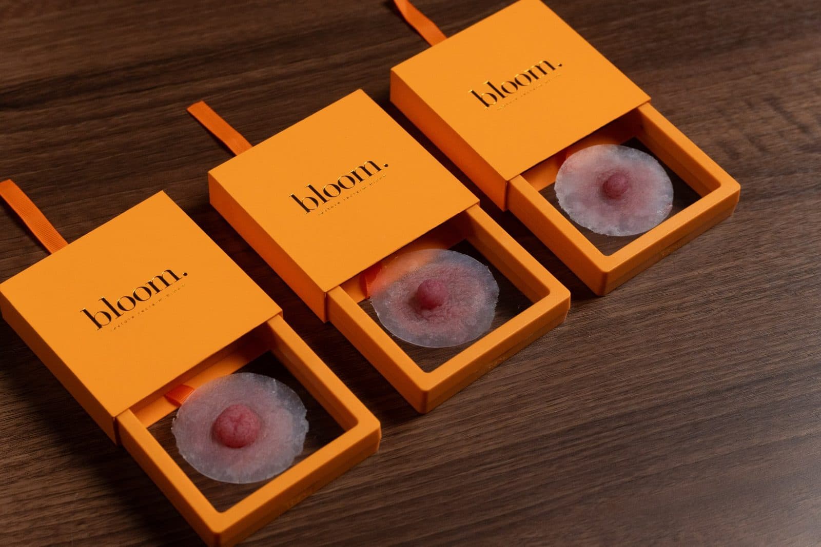 Bloom Signature in Blush: the three nipple styles side by side in open marigold boxes on dark wood. Left to right: the Unapologetic, the Authentic and the Self-Assured.
