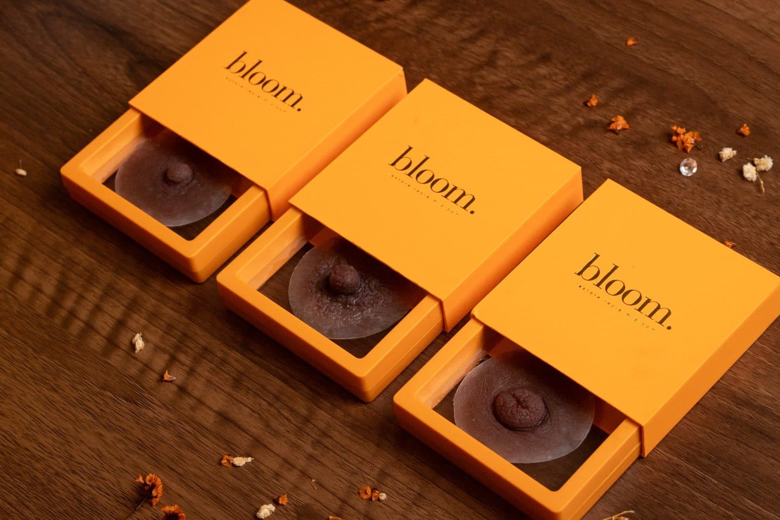 Bloom Signature in Deep Cocoa: the three nipple styles side by side in open marigold boxes on dark wood. Left to right: the Self-Assured, the Authentic and the Unapologetic.