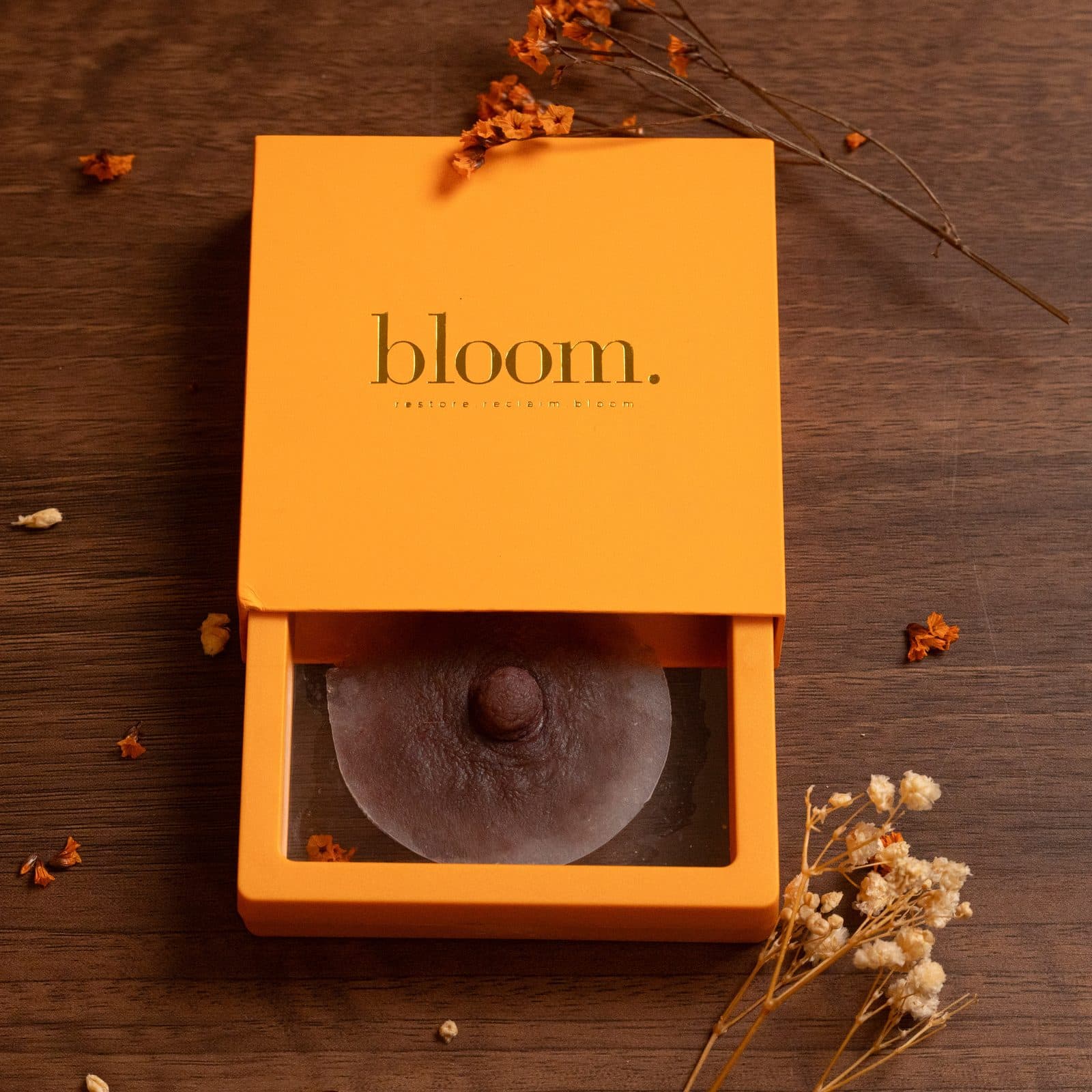 A Bloom piece in a deep shade in the open drawer of its marigold box, with dried gypsophila on dark wood.