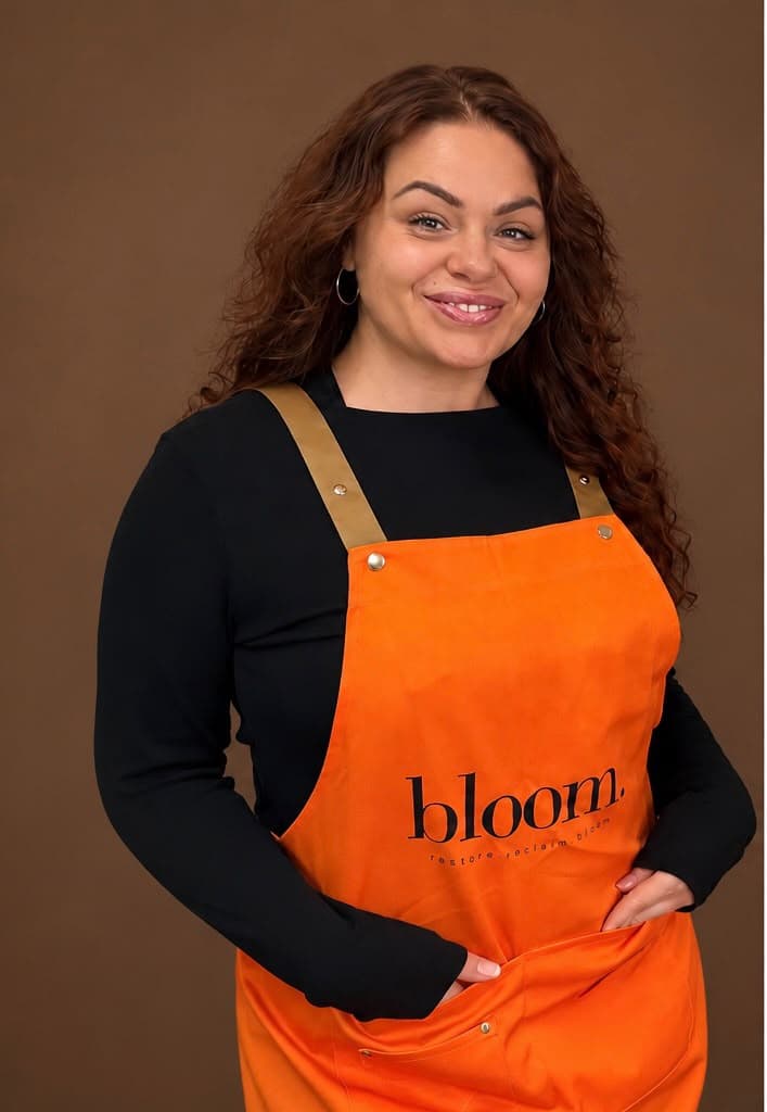 Megan Jones, Bloom artist in Durham, smiling in a marigold Bloom apron.